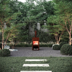 Tall outdoor Mac Landscape's Heat Haven fire pit in a garden setting with trees and rocks.