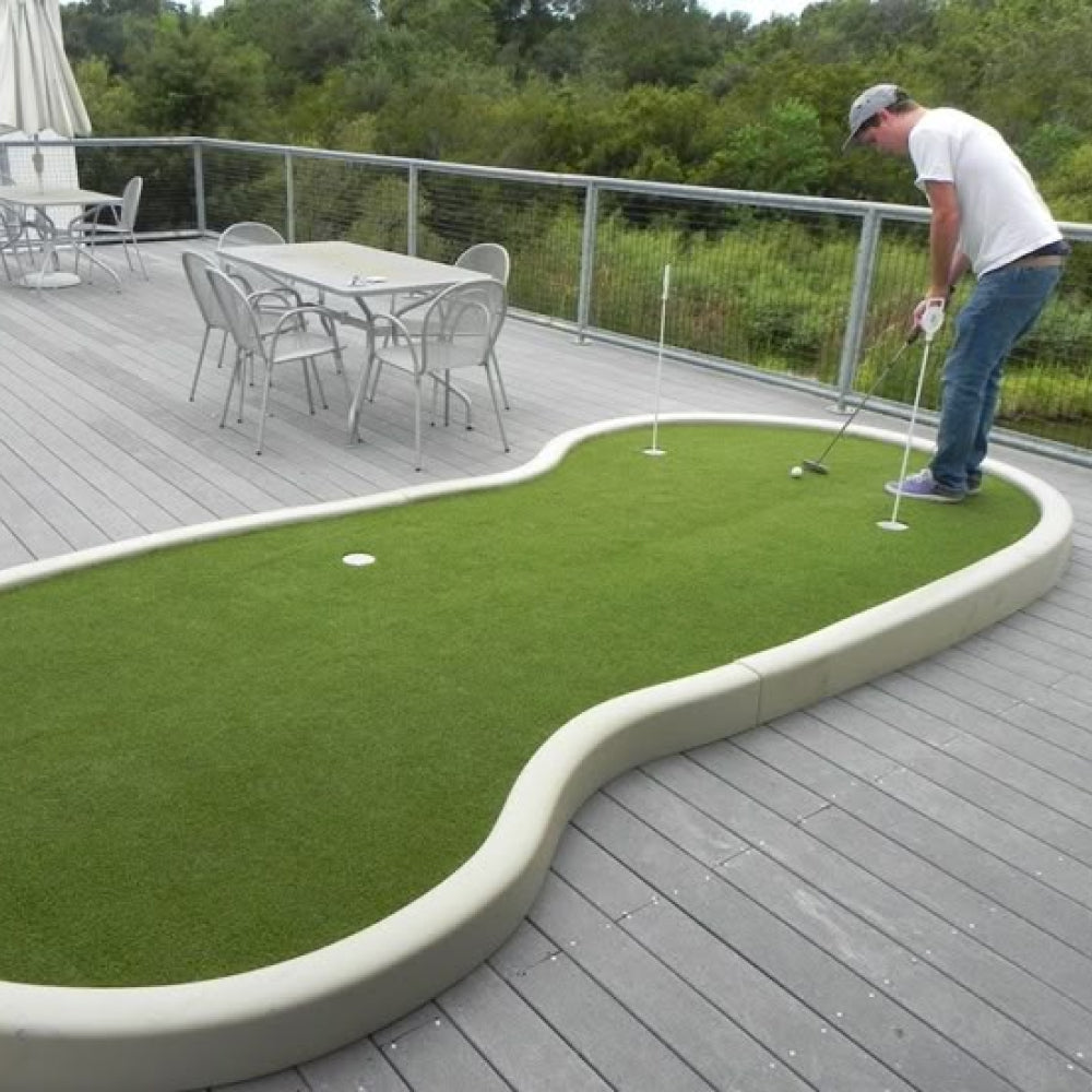 Person playing mini golf on a green artificial set up with a in the background.