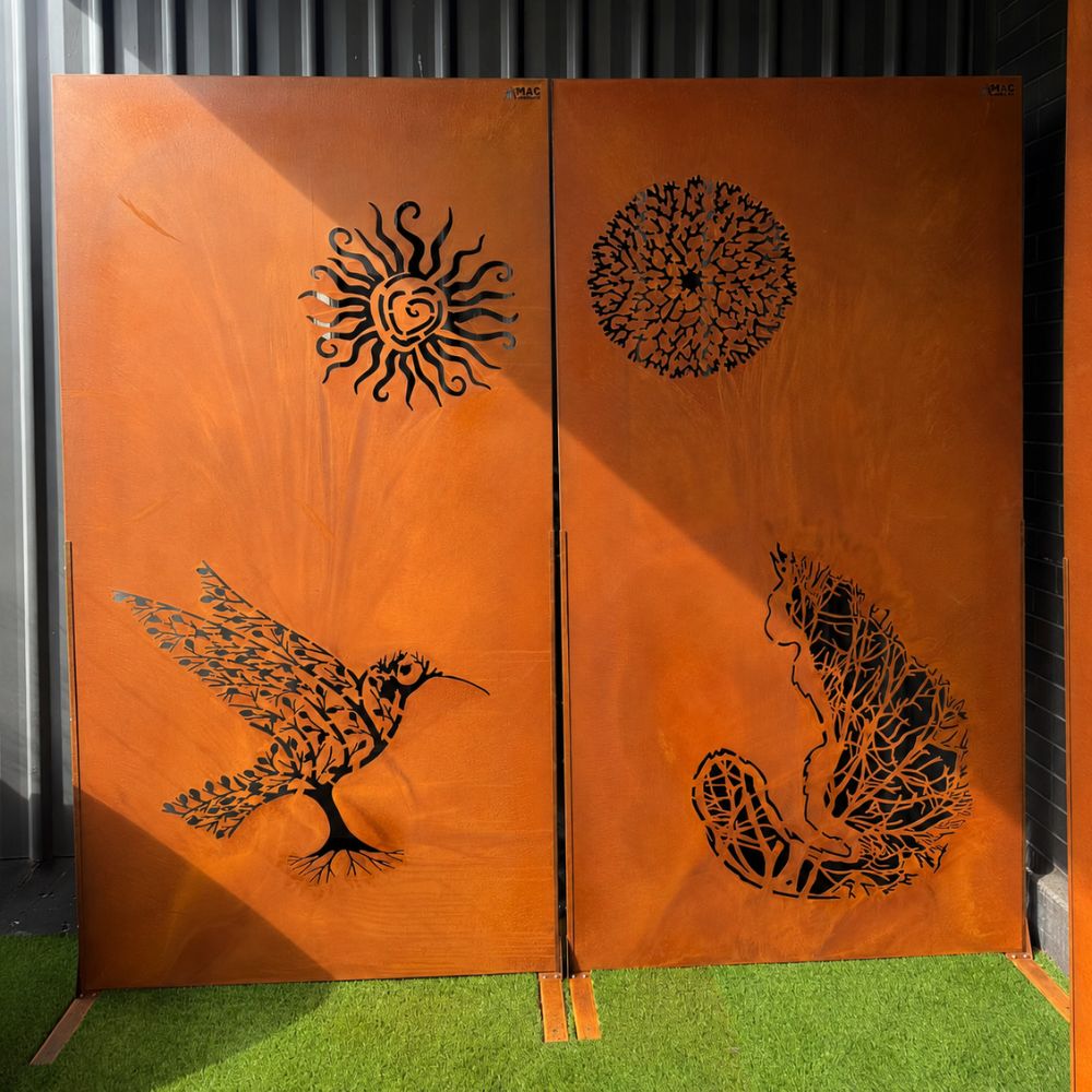 Corten Steel Felix Screen featuring decorative laser-cut artwork of a cat, hummingbird, sun, and botanical-inspired patterns on rust-finished steel panels. Freestanding on a lawn, the contemporary privacy screen adds artistic character, stylish screening, and architectural interest to modern outdoor gardens and landscaped spaces.